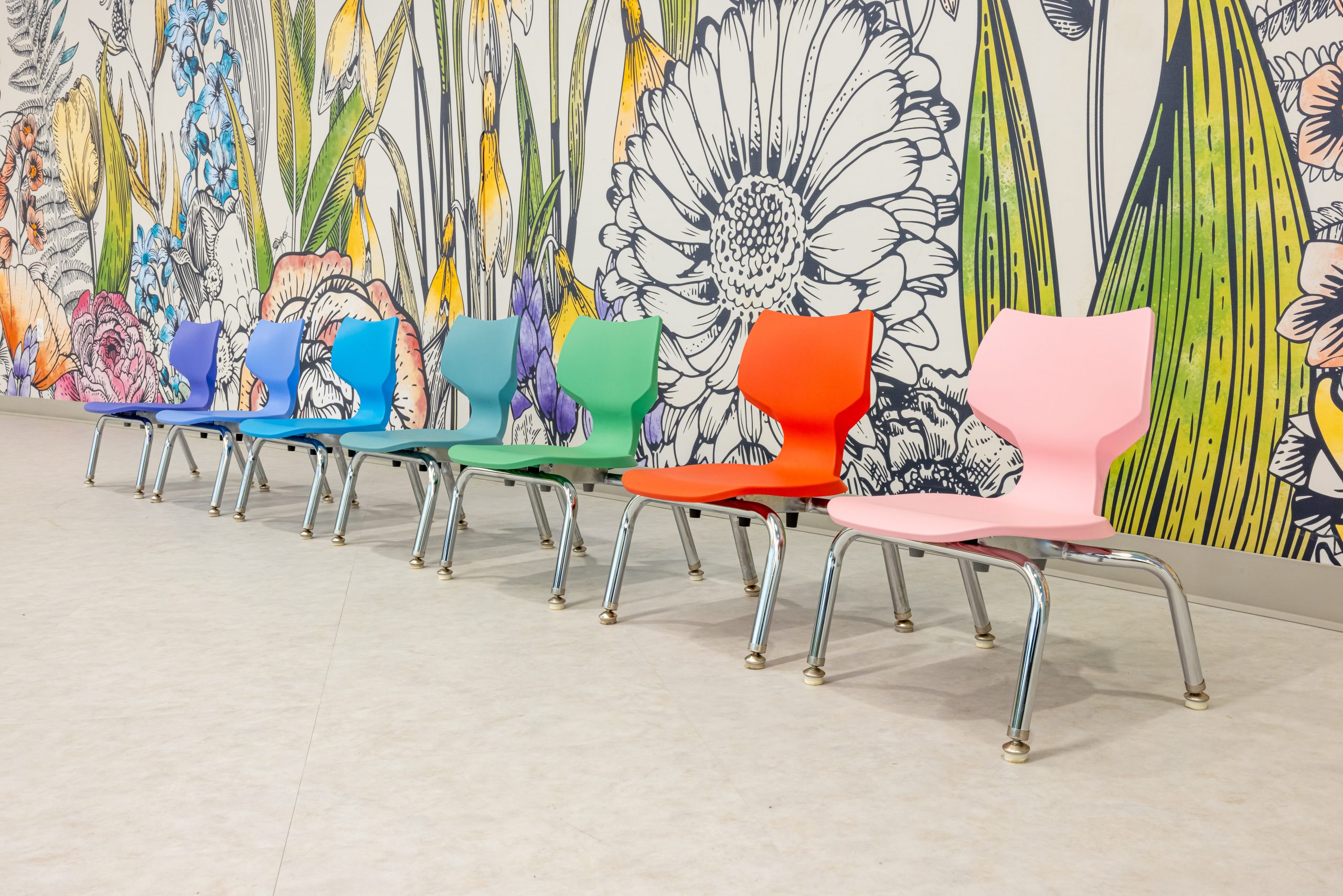 a series of child size chairs in multiple colors against a floral mural