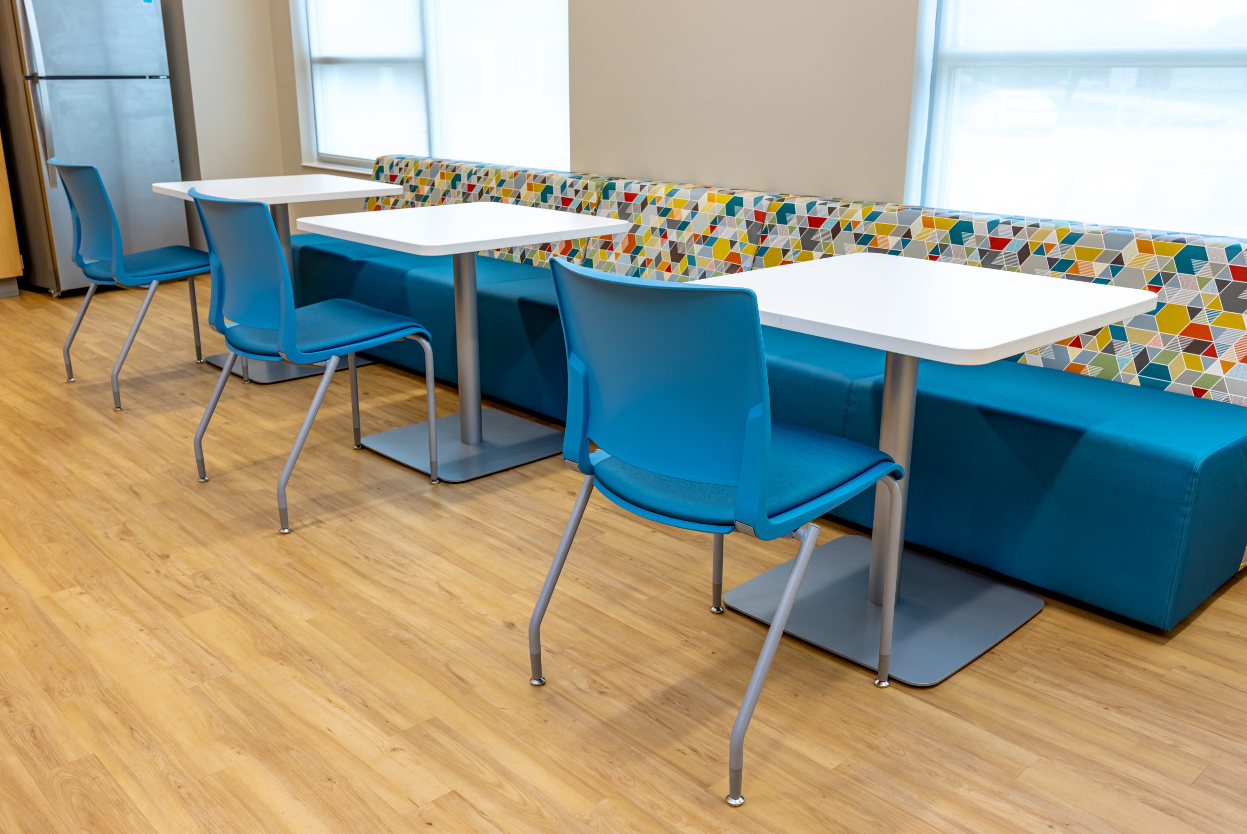 a lounge area for adults with colorful bench seating, cafe tables and blue chairs