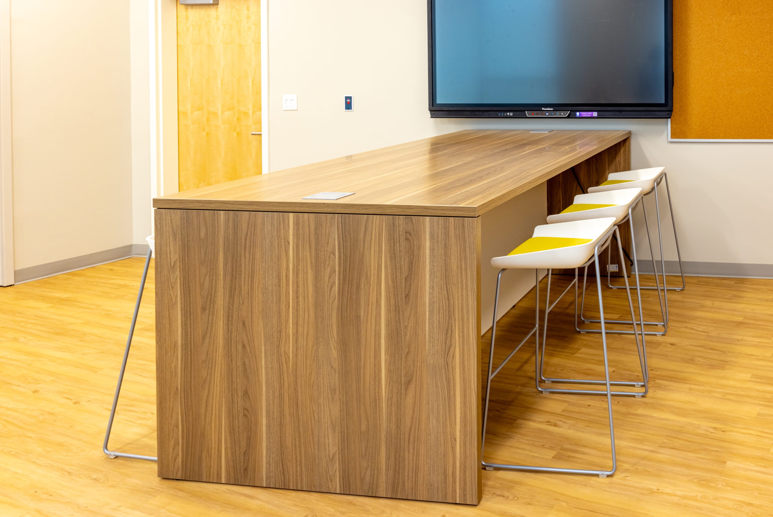a meeting area featuring a large wooden table, stools and a television mounted on the wall