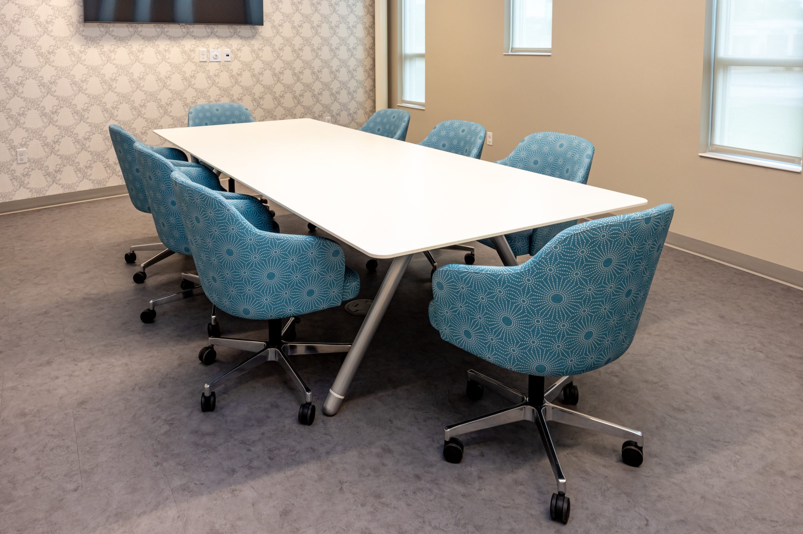 a white conference room table with 8 blue conference chairs on casters