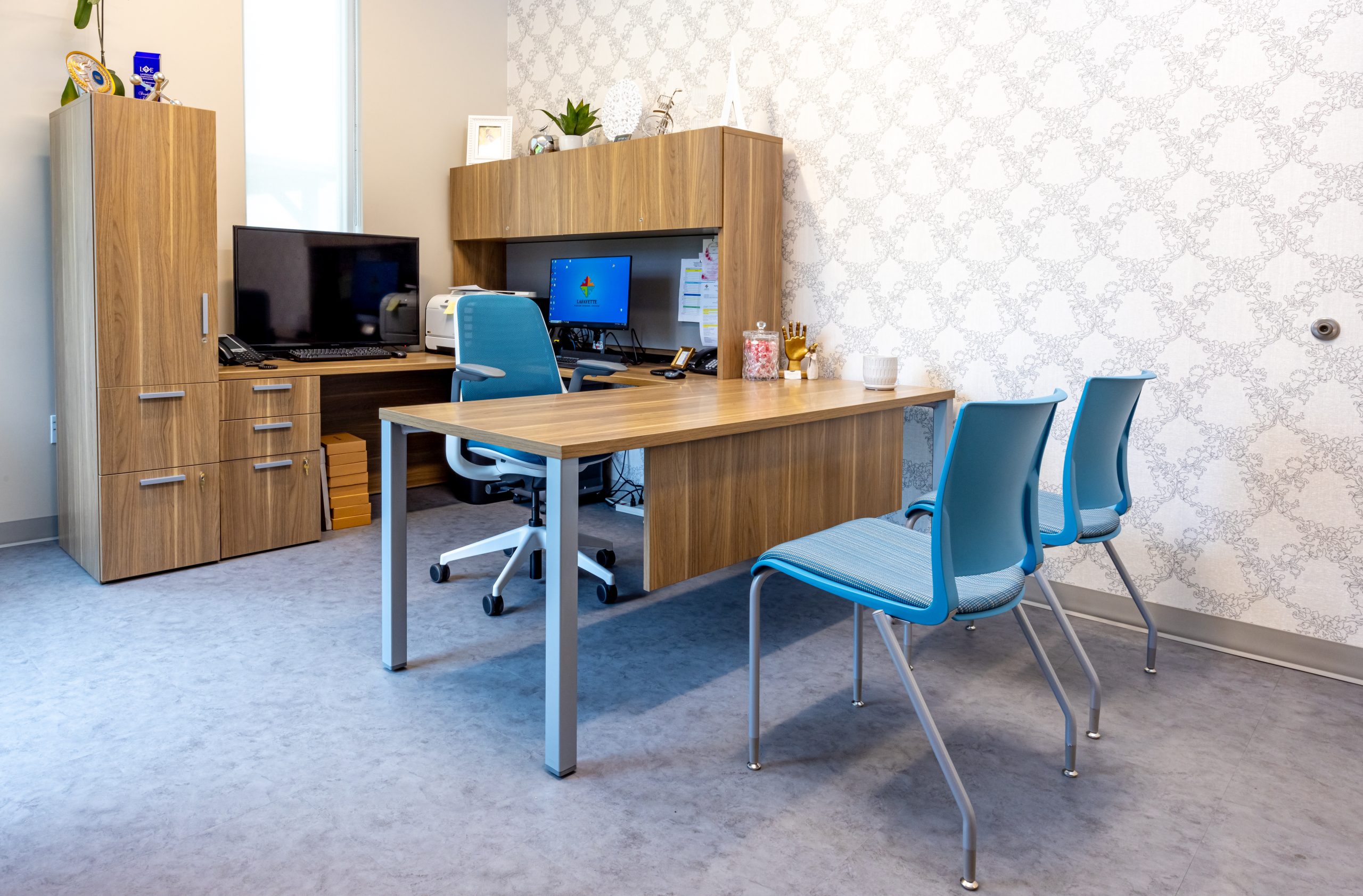 an administrators office featuring a wooden desk and cabinetry, office chair and 2 guest chairs