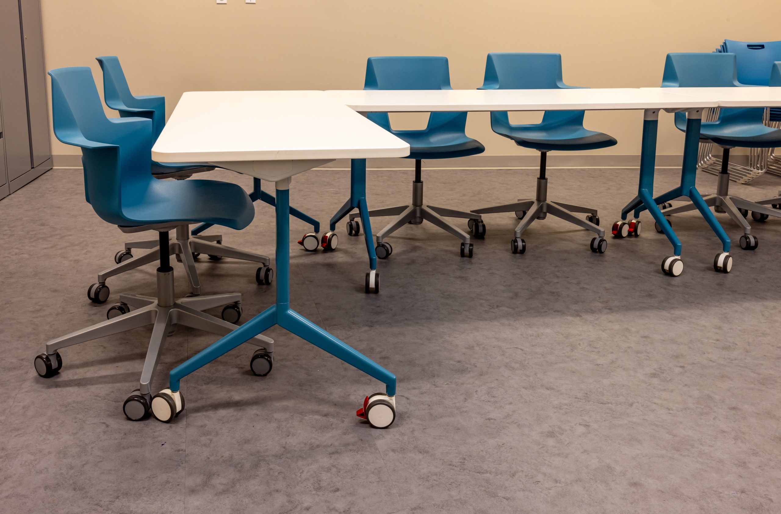 L-shaped meeting table on casters with multiple blue chairs on casters