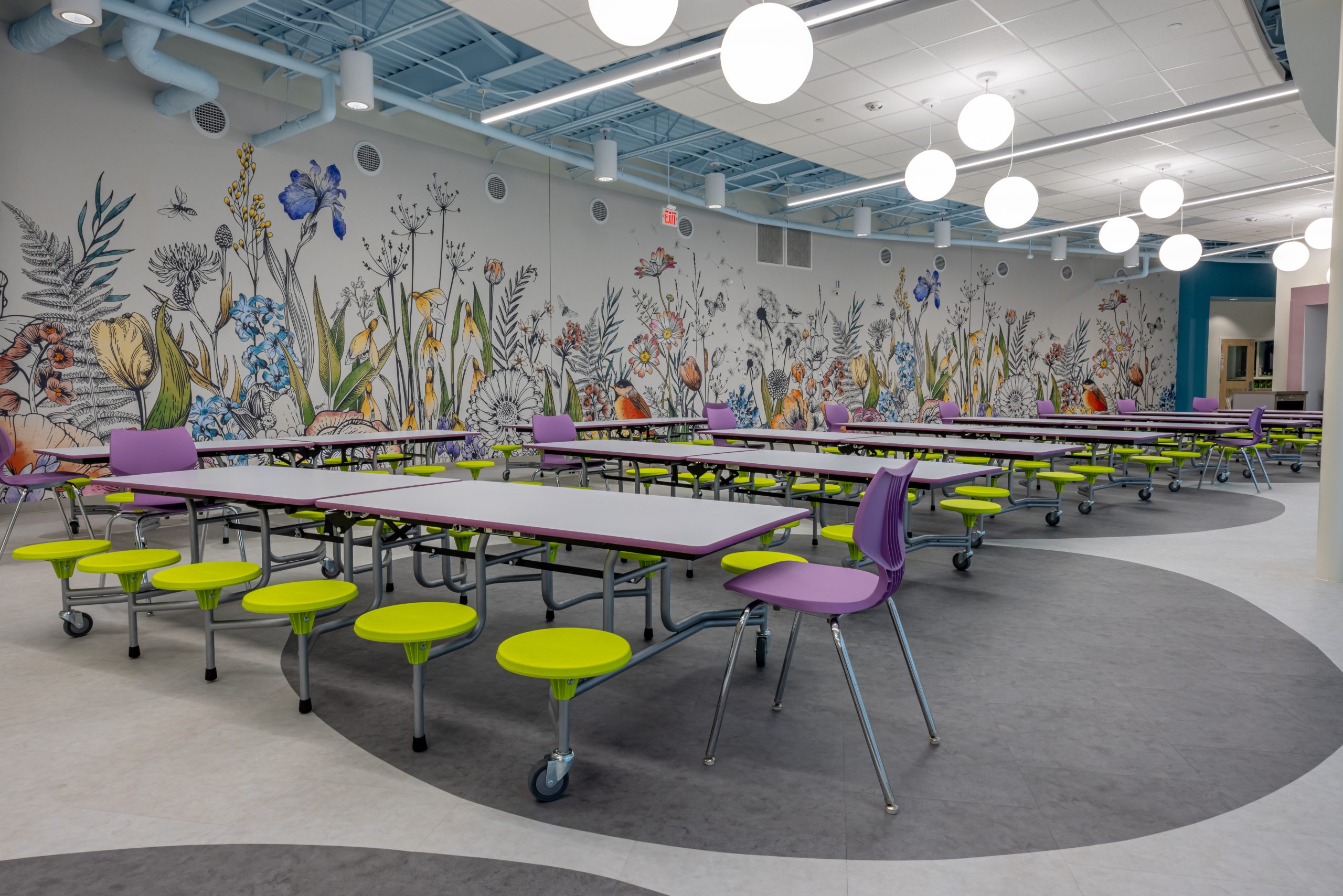 interior of a preschool cafeteria with rows of tables, stools and teacher chairs